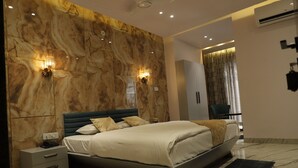 A modern bedroom with a marble wall, a bed with white linens, two wall-mounted lights, a nightstand, and a black rug. - Hotel Shree Darshnam (Mathura)