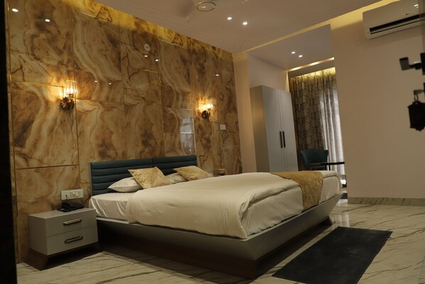 Une chambre moderne avec un mur en marbre, un lit recouvert de linge de maison blanc, deux lampes fixées au mur, une table de chevet et un tapis noir.
