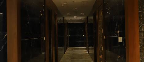 A corridor with marble flooring and wooden columns, leading to a dark room.