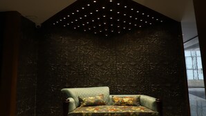 A modern interior with a geometric-patterned wall, a green upholstered sofa with floral cushions, and a ceiling with recessed lighting. - Hotel Shree Darshnam (Mathura)