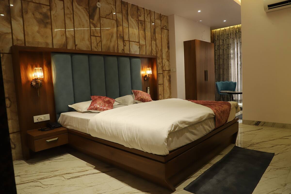 A modern hotel bedroom with a large bed, wooden headboard, and two wall-mounted lights.