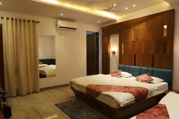 A modern hotel room with a large bed, a wooden headboard, a mirror, and an air conditioning unit. - Hotel Shree Darshnam (Mathura)