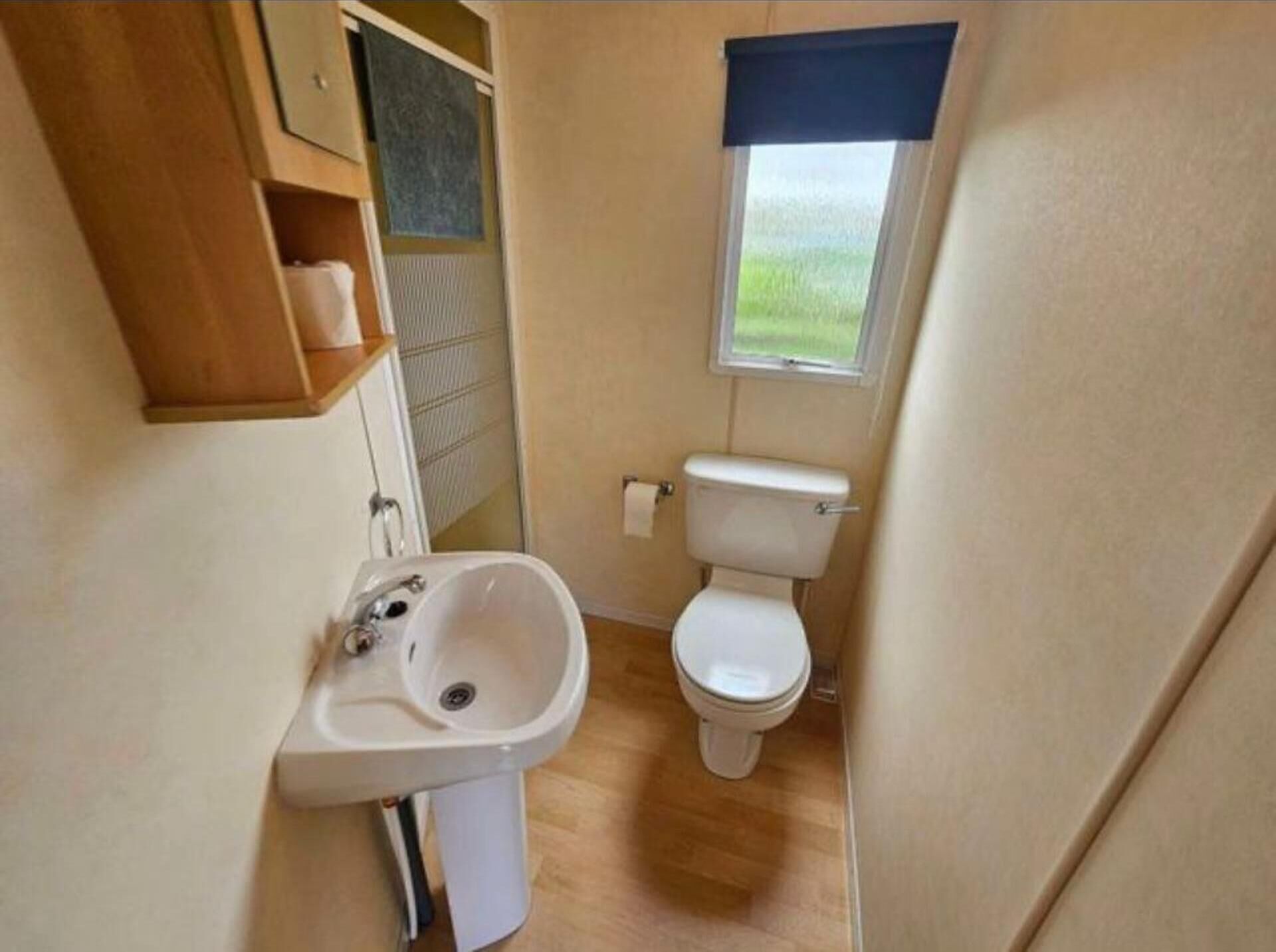 A compact bathroom with a sink, toilet, and a window providing a view of the outdoors.
