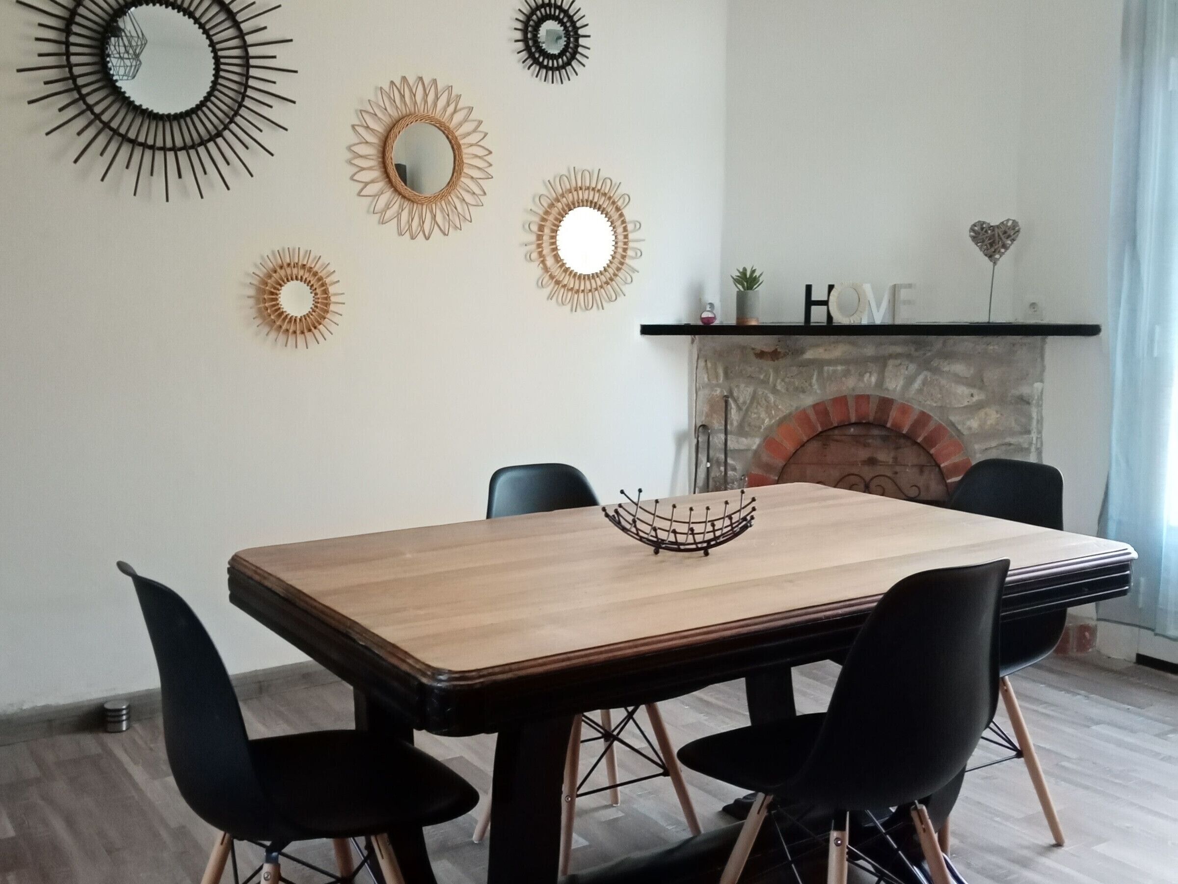 Un coin repas avec une table en bois et des chaises noires, une cheminée et des miroirs décoratifs fixés au mur.