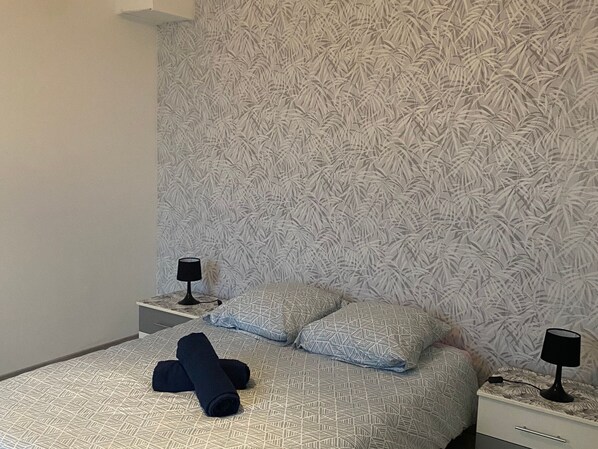 Una cama bien hecha con ropa de cama estampada, dos mesitas de noche con lámparas, y una pared decorada con un diseño de hojas.