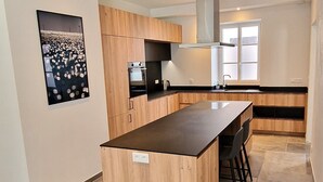 A modern kitchen with wooden cabinets, a central island, and a built-in oven. - Renovated house in the heart of Groix, 9 sleeps (Groix)