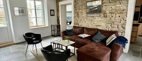 Ein Wohnzimmer mit Steinwand, braunem Ledersofa, schwarzem Sessel und kleinem Tisch.