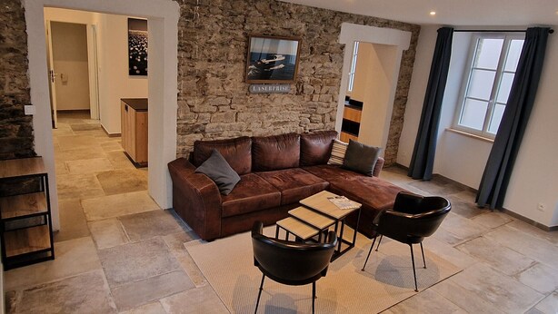 A modern living room with a stone wall, a brown leather sofa, two black chairs, and a wooden coffee table. - Renovated house in the heart of Groix, 9 sleeps (Groix)