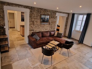 A modern living room with a stone wall, a brown leather sofa, two black chairs, and a wooden coffee table. - Renovated house in the heart of Groix, 9 sleeps (Groix)
