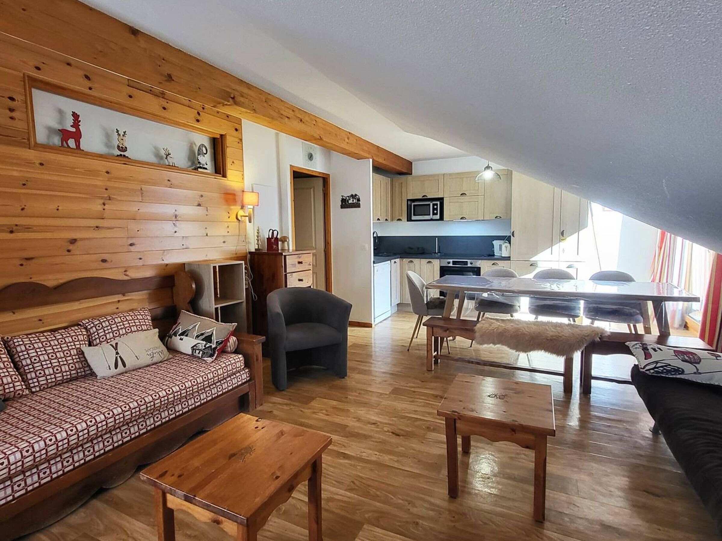 A cozy living area with a wooden sofa, a coffee table, and a dining table with chairs. A kitchen with a microwave and cabinets is visible in the background.