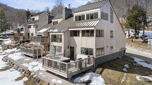 Une cabane moderne avec des fondations en pierre, une terrasse en bois et un jacuzzi.