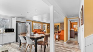 Une cuisine moderne avec des meubles blancs, un coin repas doté d’une table et de chaises en bois, et un salon avec un canapé orange.