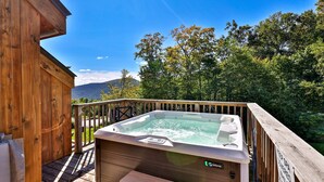 Une terrasse en bois avec un jacuzzi et une vue sur une forêt et des montagnes.