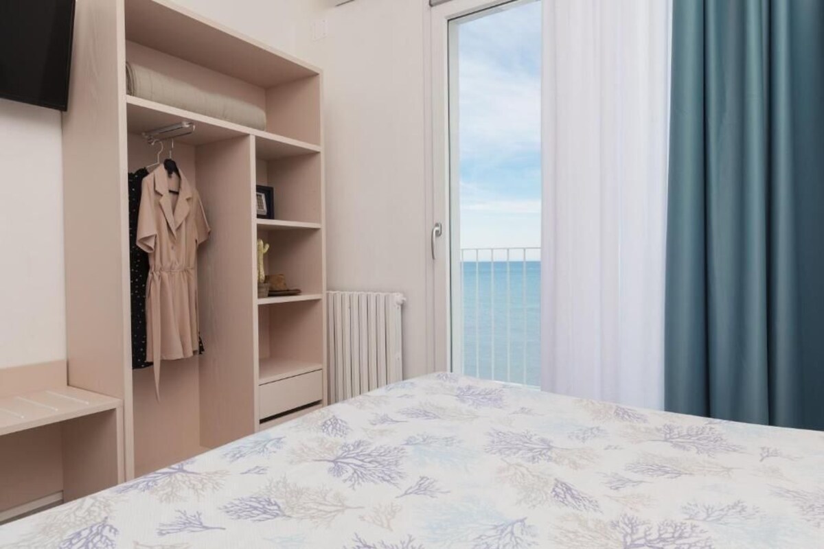 A bedroom with a bed, a wardrobe, and a view of the sea through a sliding door.