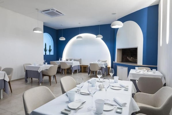 Un comedor moderno con mesas dispuestas para el servicio, que presenta una decoración en tonos azul y blanco e iluminación contemporánea.