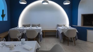 Un comedor con mesas redondas, manteles blancos y lámparas colgantes.