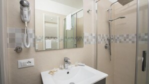 Un baño moderno con cabina de ducha de vidrio, secador de pelo montado en la pared y lavabo con artículos de aseo.