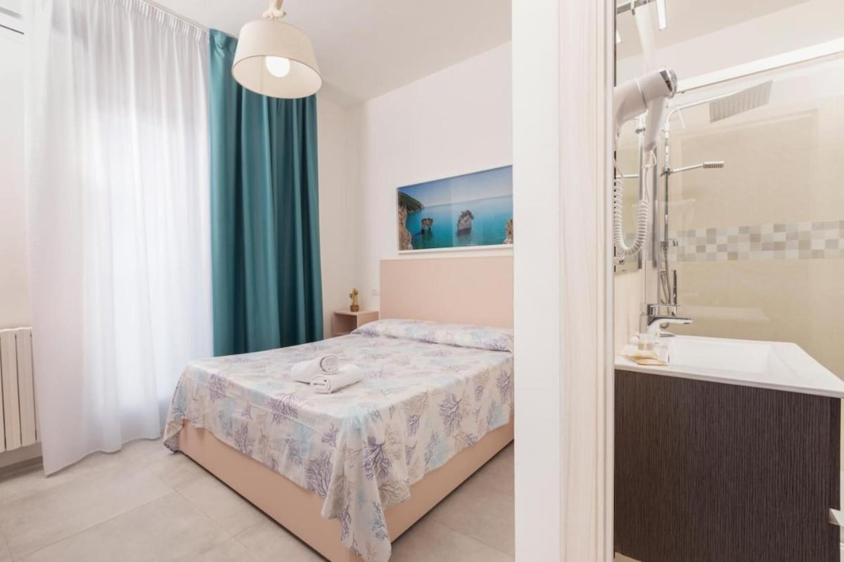 Ein Schlafzimmer mit Bett, Nachttisch, einem Gemälde sowie einem Badezimmer mit Badewanne und Dusche.