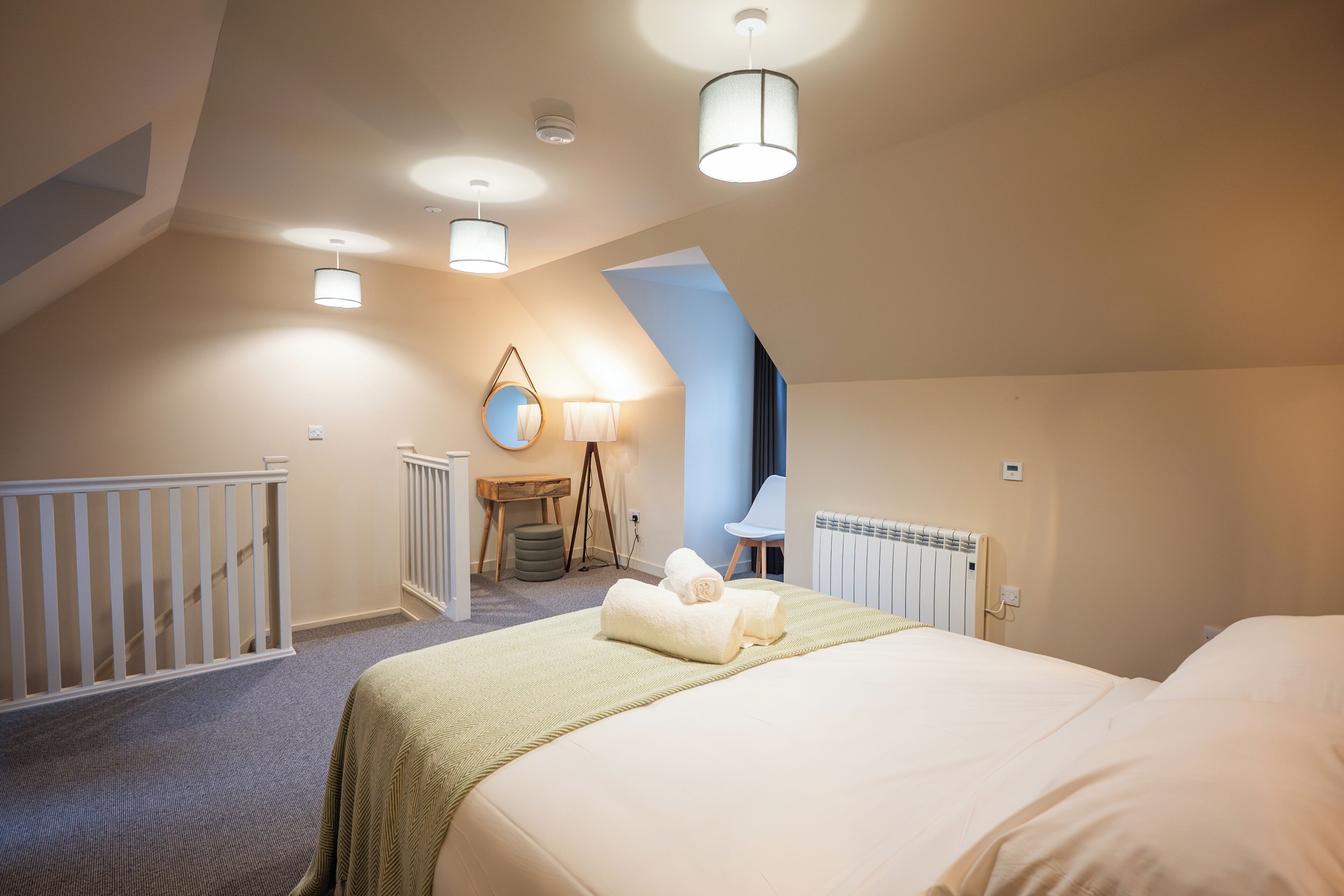 A bedroom with a large bed, a small desk, a chair, a mirror, and a radiator.