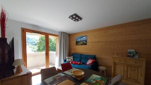Una sala de estar moderna con una pared de madera, un sofá azul, una mesa de comedor con individuales y vistas a través de una puerta de cristal.