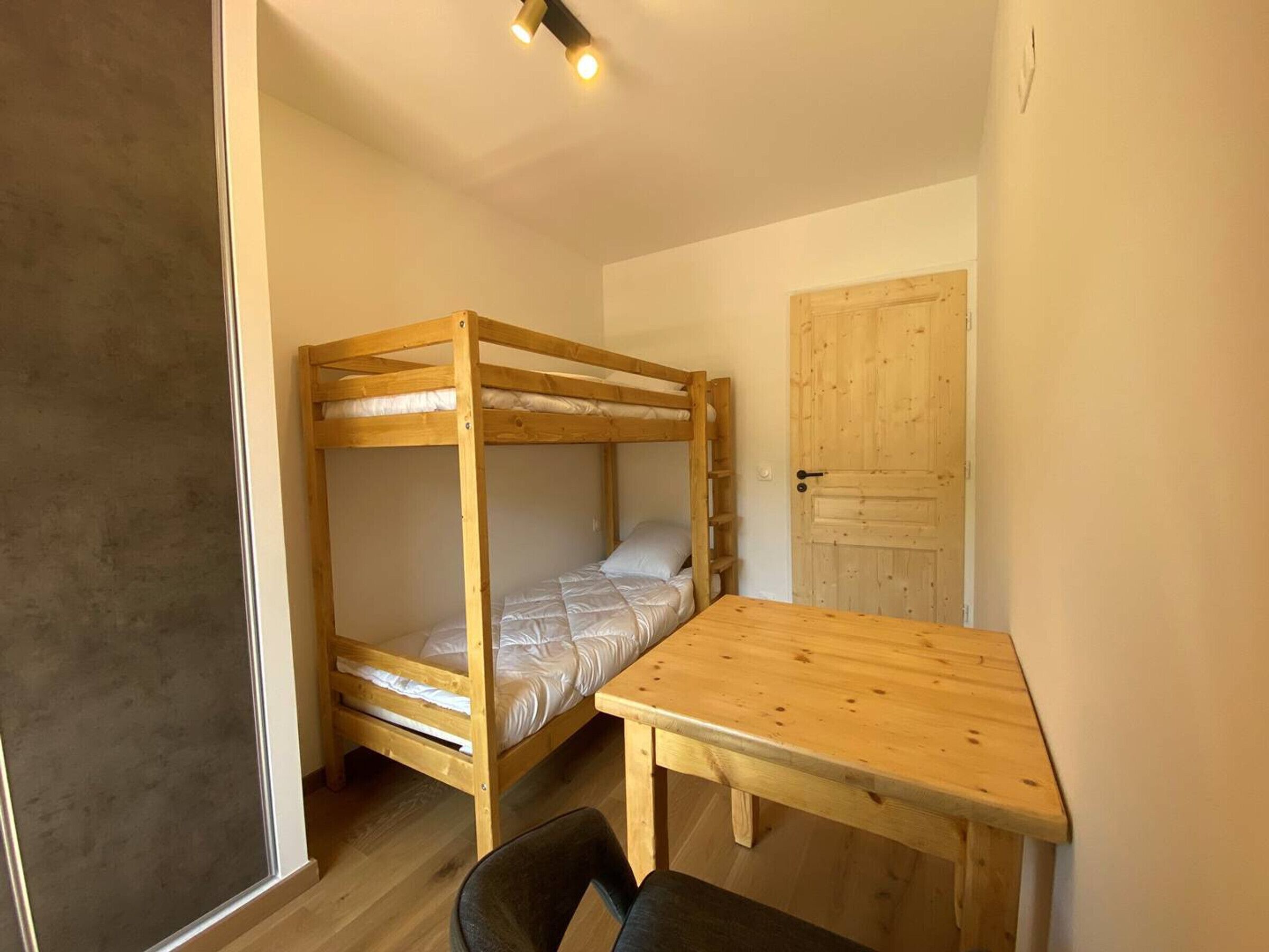 Un petit logement composé d’une seule pièce, comprenant un lit superposé, une table en bois et une porte.