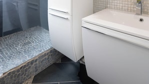 A bathroom with a white sink, a mirror with a yellow accent, and a shower area with a stone floor. - Apartment "Maya" - 2-4 guests - Lake view, near the centre (Gérardmer)
