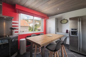A modern kitchen with a wooden dining table, black chairs, a stainless steel refrigerator, and a window with a view of houses. - Apartment "Maya" - 2-4 guests - Lake view, near the centre (Gérardmer)