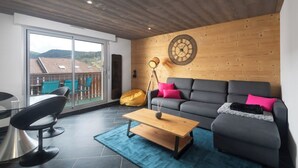 A modern living room with a grey sofa, a wooden coffee table, and a large window overlooking a balcony. - Apartment "Maya" - 2-4 guests - Lake view, near the centre (Gérardmer)