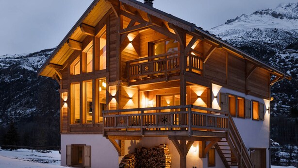 Una cabaña de madera con balcón, ventanas amplias y una escalera que lleva a un nivel superior.