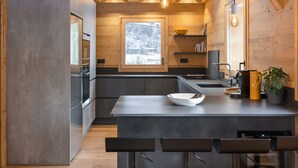 Una cocina moderna con vigas de madera, un ventanal amplio y una isla central con taburetes de bar.