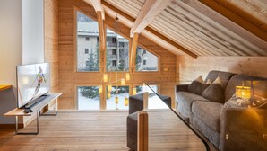 Un moderno loft con vigas de madera, ventanas amplias, sofá y televisor.
