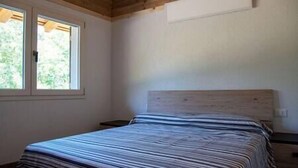 Ein Schlafzimmer mit einem hölzernen Kopfteil, einem großen Fenster und einem ordentlich bezogenen Bett.