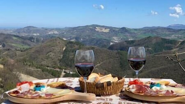 Ein Tisch mit Blick auf sanfte Hügel, zwei Gläser Rotwein und eine Auswahl an Käse und Wurstwaren.