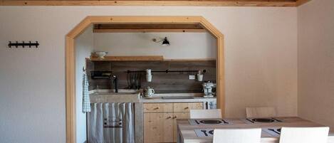 A compact kitchen with wooden beams, a dining area with a table and chairs, and a small sink.