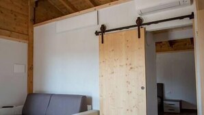 A room with a wooden ceiling, a sliding door, a grey sofa, and a white cabinet. - Straw apartment (Mercato Saraceno)