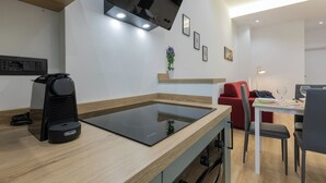 Een moderne keuken met een geïntegreerde inductiekookplaat, een koffieapparaat en een eethoek met een rode bank en een tafel gedekt voor twee.