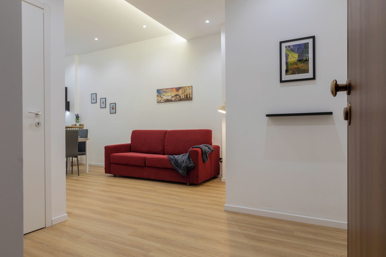 Un salon moderne avec un canapé rouge, un coin repas comprenant une table et des chaises, et un tableau accroché au mur.