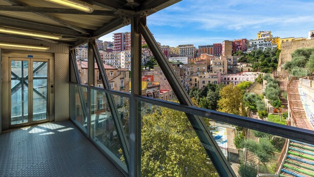 A balcony with a glass railing overlooking a cityscape with buildings and trees. - Montesanto Apartment by Wonderful ltaly (Naples)
