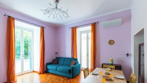 A room with a teal sofa, a dining table set with plates and glasses, and a chandelier. - Montesanto Apartment by Wonderful ltaly (Naples)