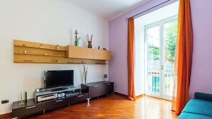 A modern living room with a flat-screen TV, wooden entertainment unit, and a sliding glass door to a balcony. - Montesanto Apartment by Wonderful ltaly (Naples)
