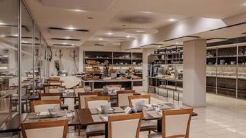 A modern dining area with tables and chairs, a buffet with various food items, and shelves with glassware.