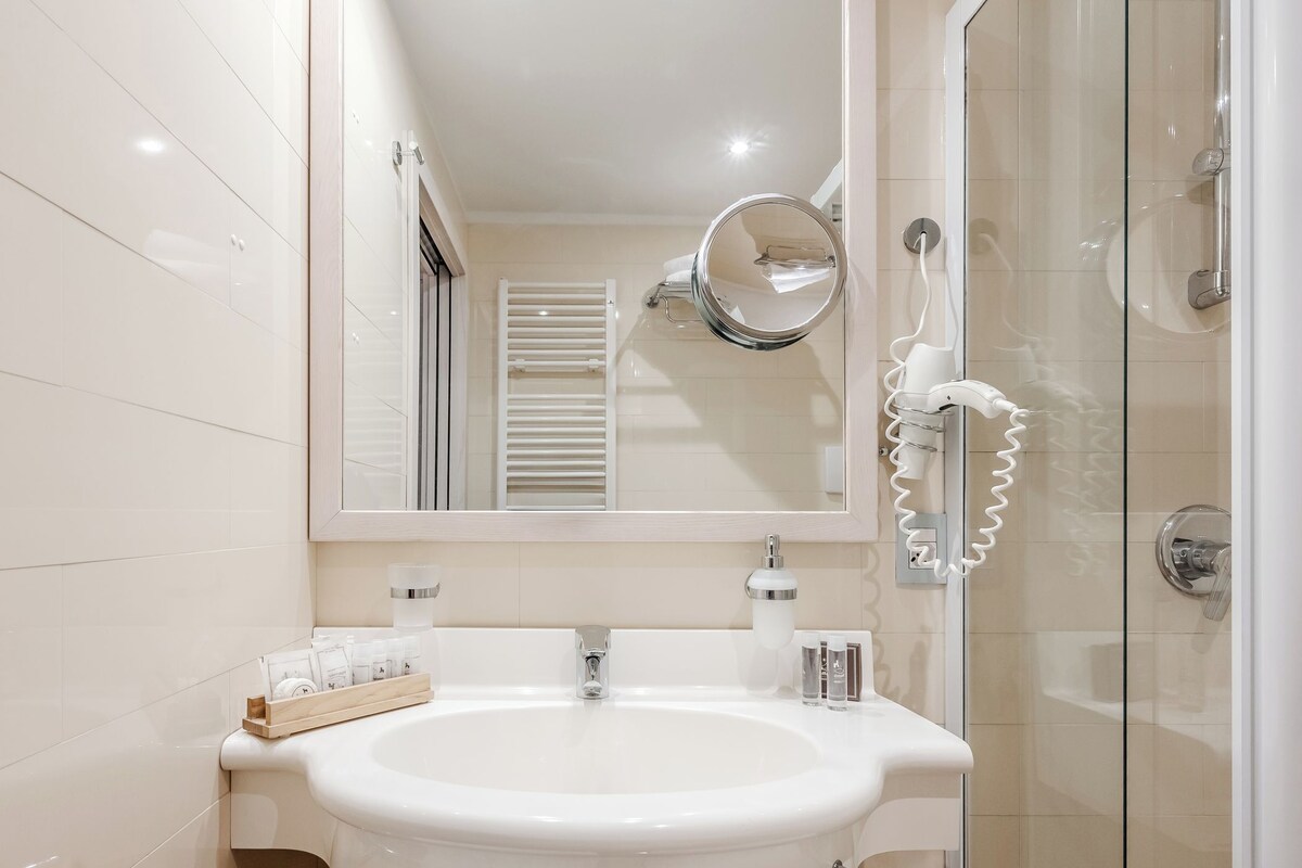 A modern bathroom with a white sink, mirror, and glass shower enclosure.