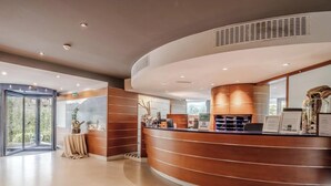 A hotel reception area with a curved reception desk, a glass elevator, and a view of the outdoors. - Hotiday Torbole Lago (Nago-Torbole)