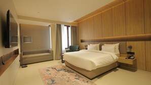Ein modernes Hotelzimmer mit einem großen Bett, einer Sitzecke mit einem Sessel, einem Flachbildfernseher und einer Wand aus Holzpaneelen.