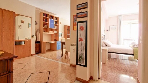 A well-lit room with a bed, a desk, and a bookshelf. There is a door leading to another room. - Cozy apartment in the heart of the Marconi district.  (Roma)