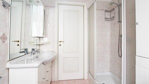 A bathroom with a white sink, a mirror, a door, and a shower area. - Cozy apartment in the heart of the Marconi district.  (Roma)