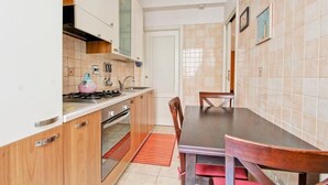 A compact kitchen with wooden cabinets, a gas stove, and a dining table with chairs. - Cozy apartment in the heart of the Marconi district.  (Roma)