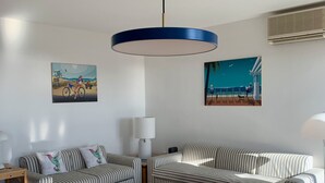 Un salon moderne avec des canapés à rayures, une table basse et une table à manger pour deux personnes. Les murs sont ornés de tableaux et le plafond est éclairé par un luminaire.