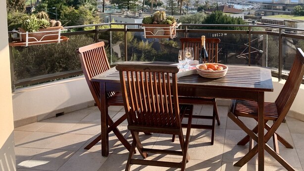 Une terrasse avec une table et des chaises, offrant une vue sur une ville côtière et les montagnes.