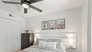 A bedroom with a bed, bedside lamps, a ceiling fan, and framed artwork on the wall. - Ivy House / 4BR Boho Retreat Near UTD (Richardson)